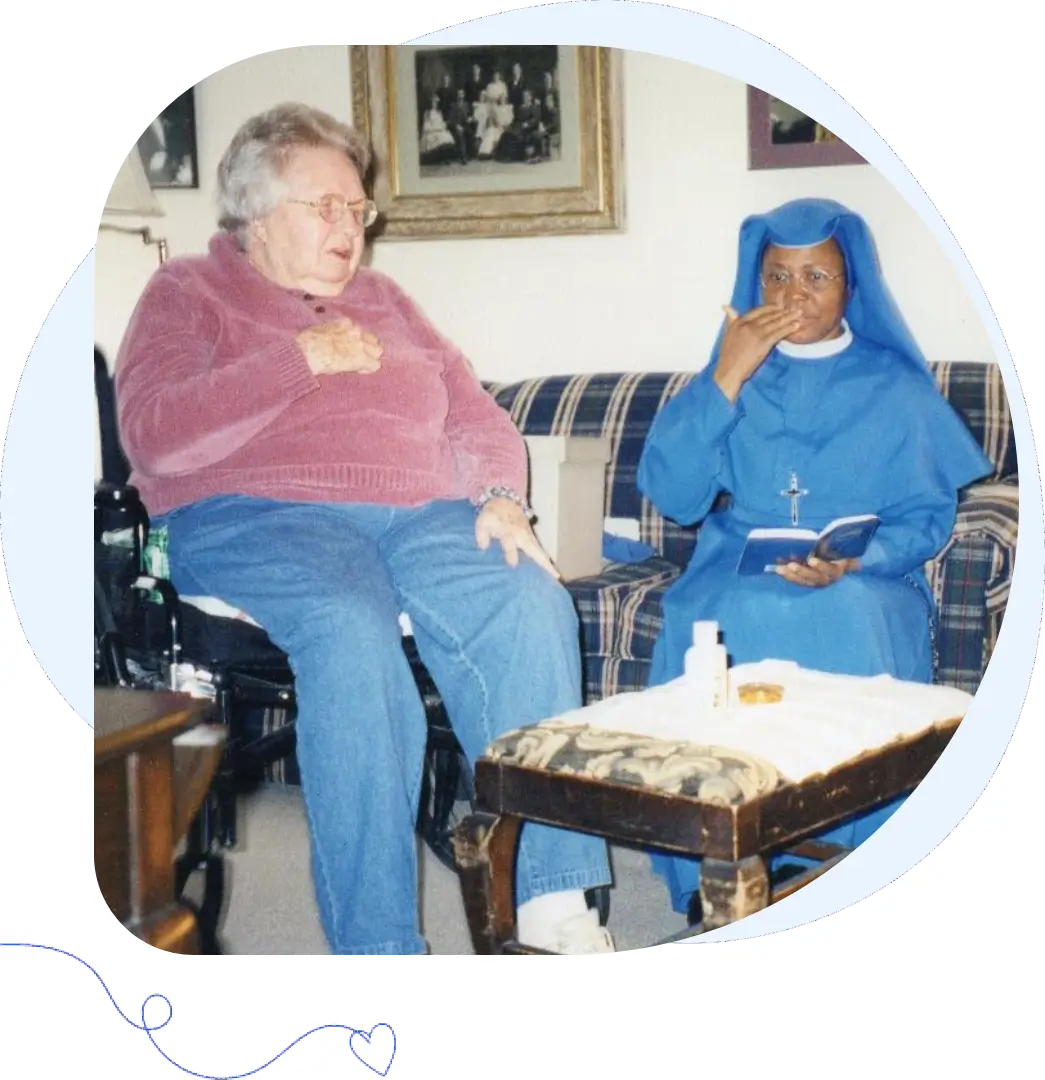 Two women sitting indoors, one elderly and one in a nun's habit.