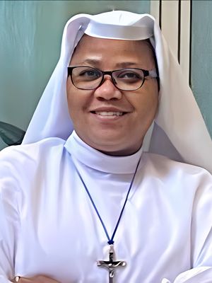 Smiling nun in white habit and glasses indoors.