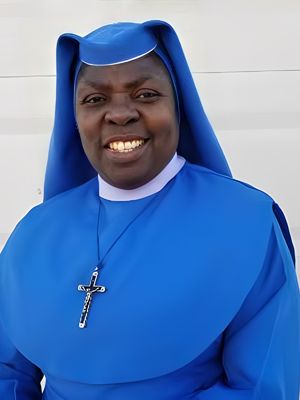 Smiling nun in a bright blue habit with a cross necklace.