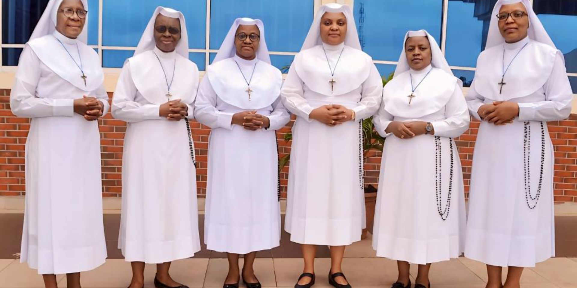 Four nuns in white habits standing and smiling in front of a blue wall.
