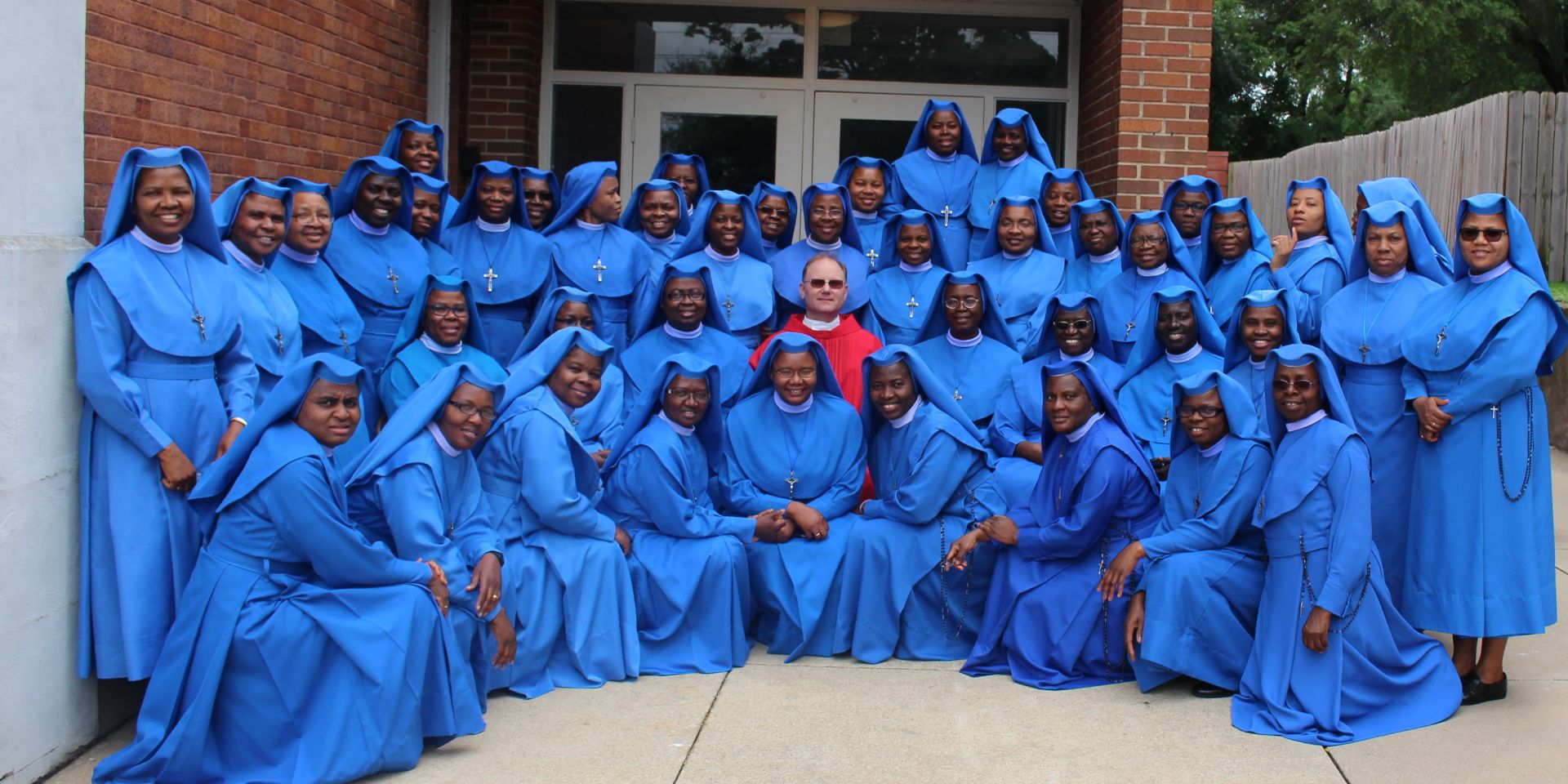A large group of women in blue choir robes posing with a man in the center.