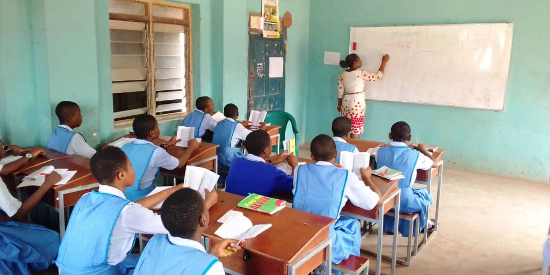 Students attentively learn from a teacher at the whiteboard in a classroom.