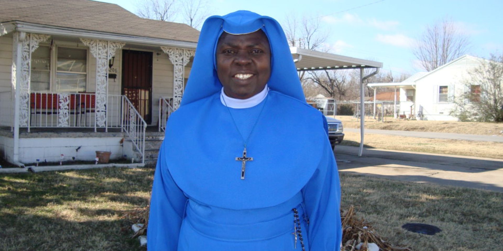 Smiling nun wearing a bright blue habit and cross necklace.