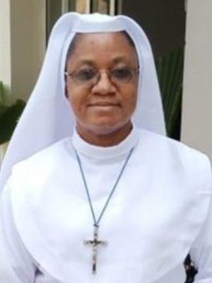 A smiling nun wearing glasses and a white habit with a cross necklace.