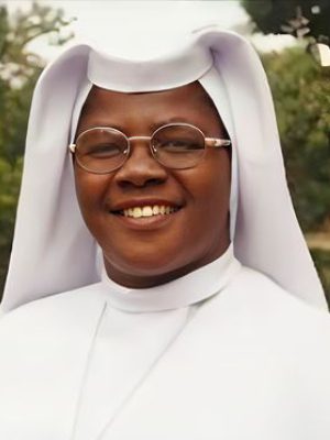 A smiling nun wearing glasses and a white habit.