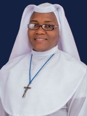 A smiling nun wearing glasses and a white habit with a cross necklace.