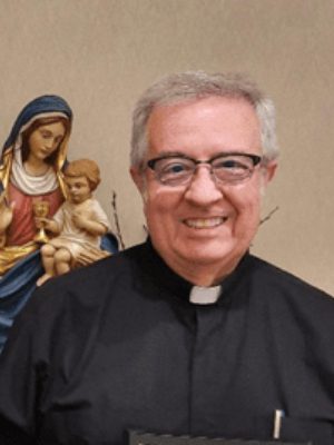 Smiling priest posing with a statue of Mary and baby Jesus.