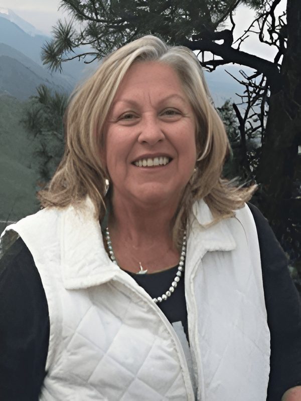 Smiling woman outdoors wearing a white vest and pearl necklace.