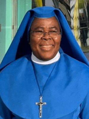Smiling nun in a blue habit and glasses.