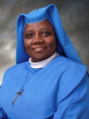 A smiling nun dressed in a blue habit and veil.