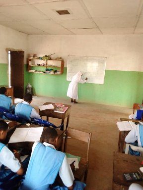 Teacher instructing students in a classroom with green walls.