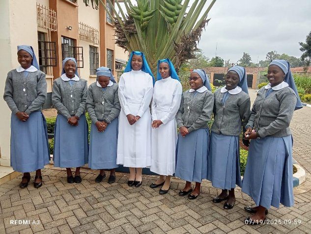 Group of nuns in grey and white habits standing outdoors near palm trees.