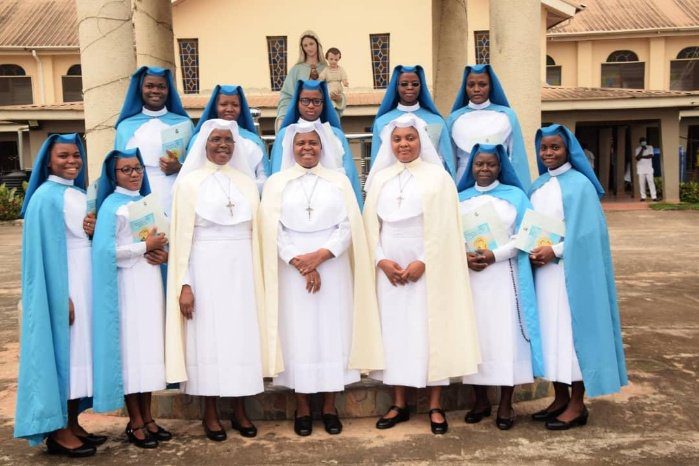 Group of nuns dressed in white and blue habits posing outdoors.