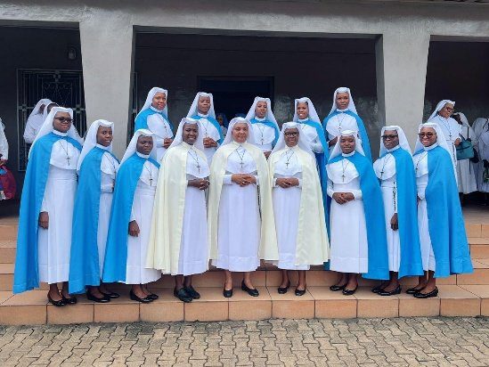 Group of nuns in white and blue habits standing outdoors.
