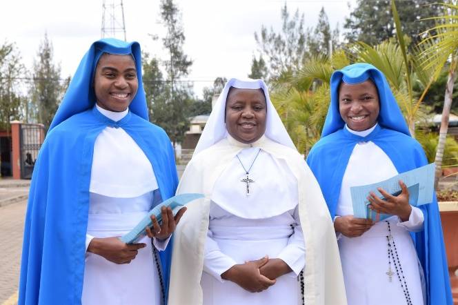 Three smiling nuns dressed in blue and white habits outdoors.
