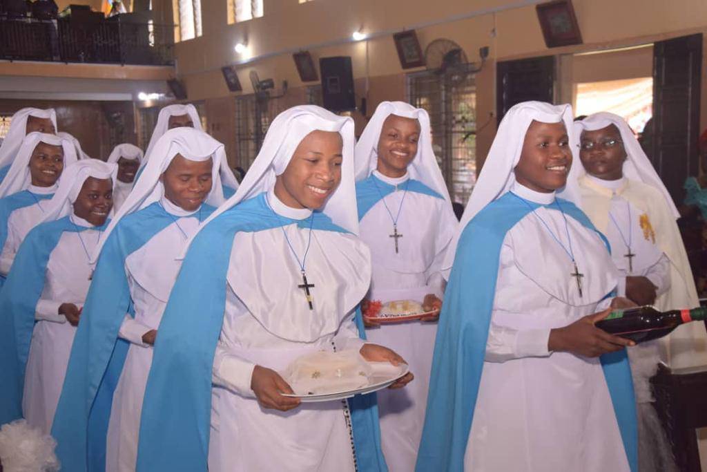 Nuns in blue and white habits smiling and holding papers inside a church.