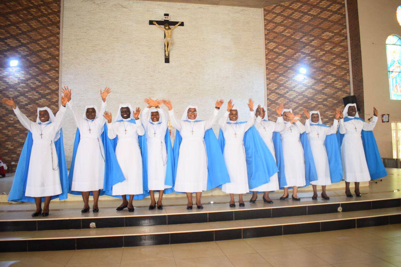 Nuns in white and blue habits joyfully raise their hands inside a church.