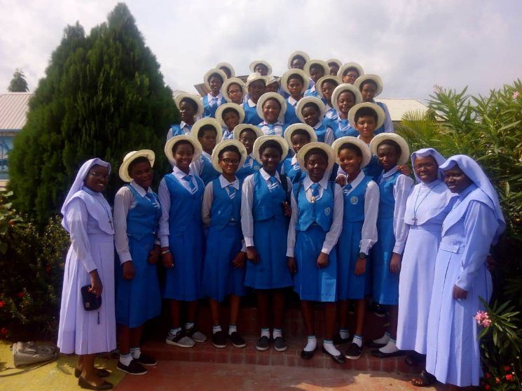 Group of women in blue uniforms and hats posing outdoors with nuns.