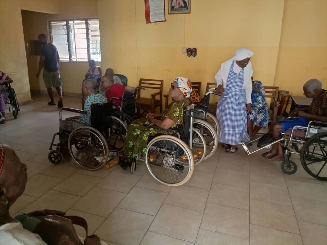 Group of elderly people in wheelchairs inside a room with a caregiver.