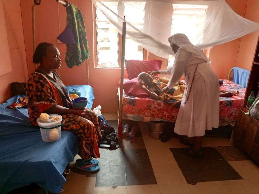 A nurse attends to a patient in a modest room with a woman watching.