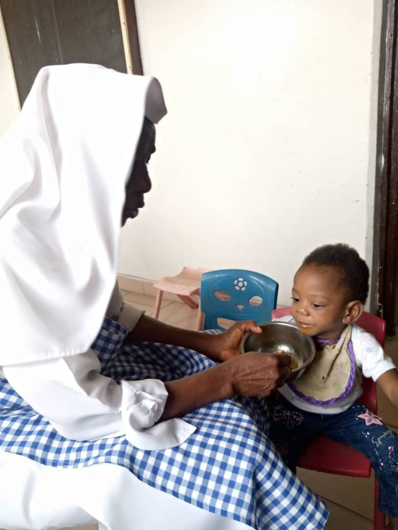 Woman in white headscarf feeding a young child with a spoon.