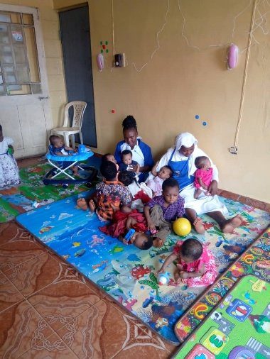 Group of children and adults sitting on colorful mats indoors.