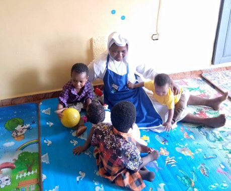 A woman and children playing with a yellow ball indoors.