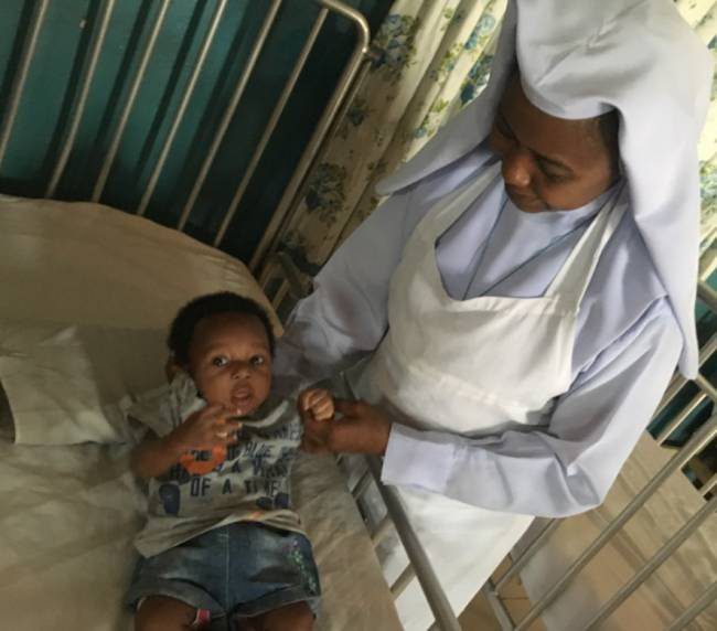 A nurse wearing a white uniform caring for a young child in a hospital bed.