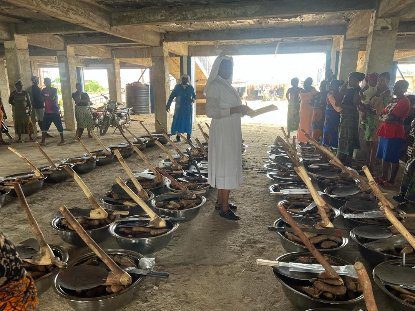 People cooking large meals outdoors in multiple pots under a rustic shelter.