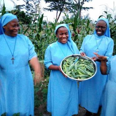 Three smiling nuns holding fresh green vegetables in a garden.