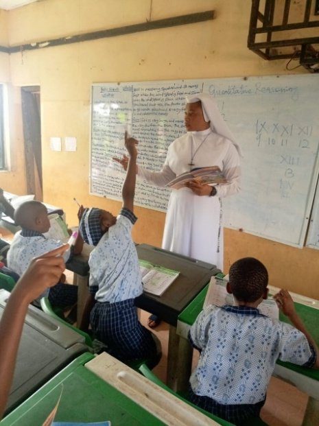 A nun teaching students in a classroom raising their hands.