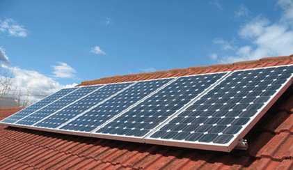 Solar panels installed on a red-tiled roof under a clear blue sky.
