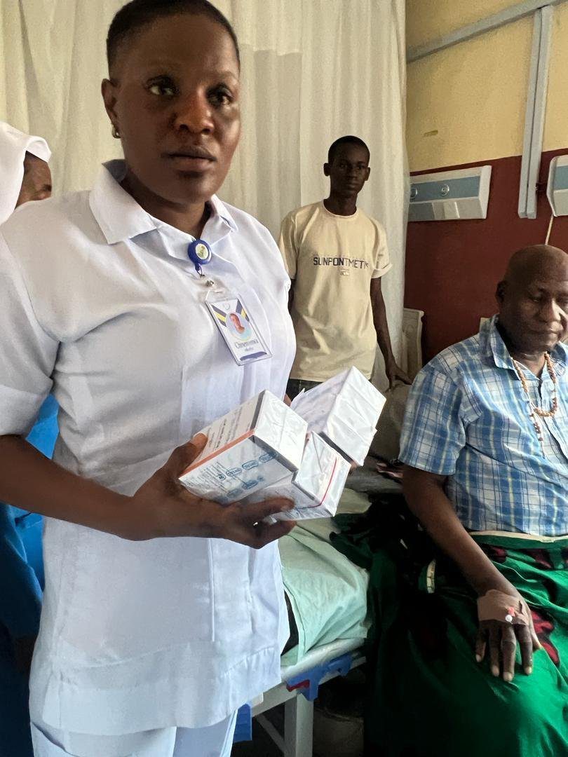 A nurse holding medical supplies beside an elderly patient in a hospital room.