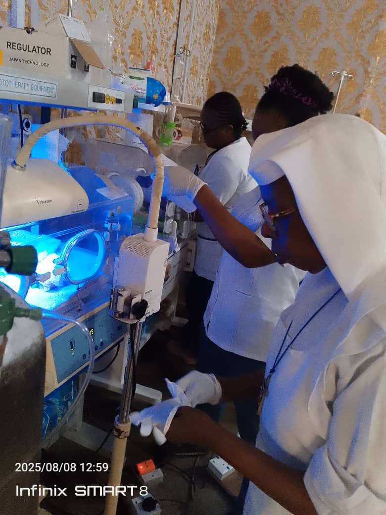 Healthcare workers attend to a baby in an incubator under blue light treatment.