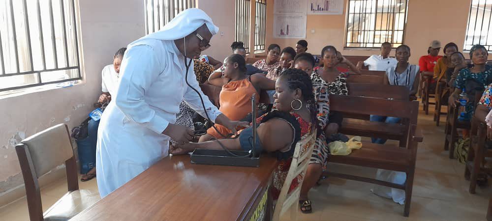 A nurse checks blood pressure of a woman in a crowded clinic.