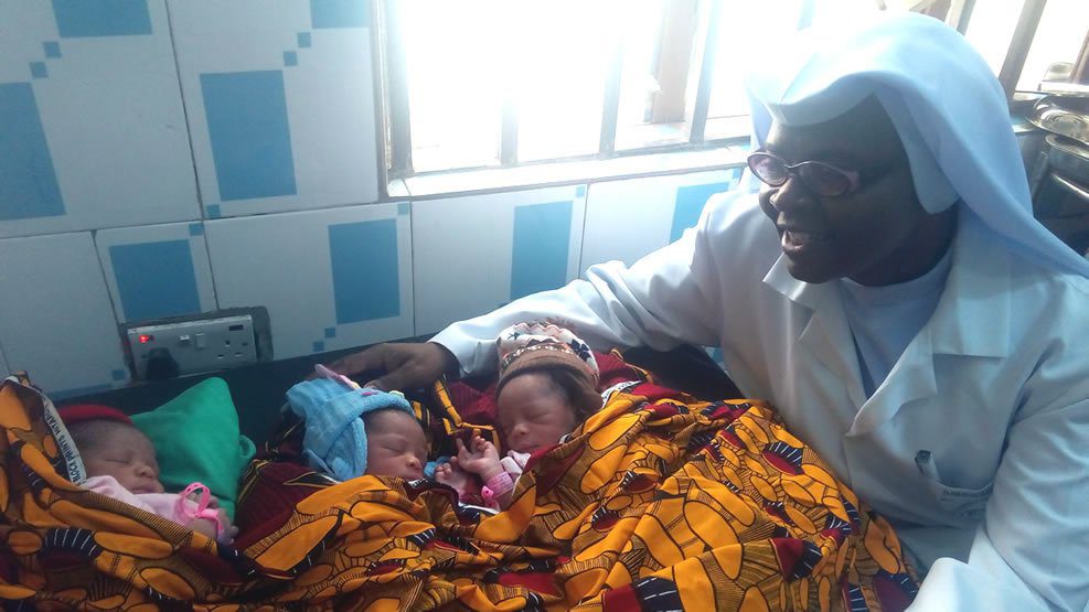 A man joyfully watches over two newborn babies wrapped in colorful blankets.