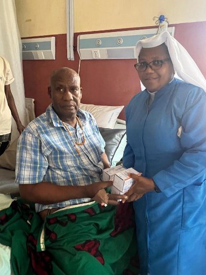 A man in a wheelchair receiving a gift from a woman in a blue habit.