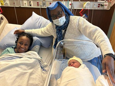 A joyful grandmother with two newborns in a hospital room.