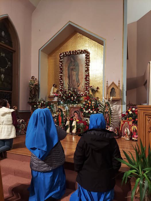 Children in blue hoodies watching a nativity scene inside a church.