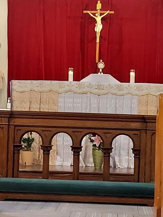 Altar with ornate wooden front and floral arrangements beneath it.