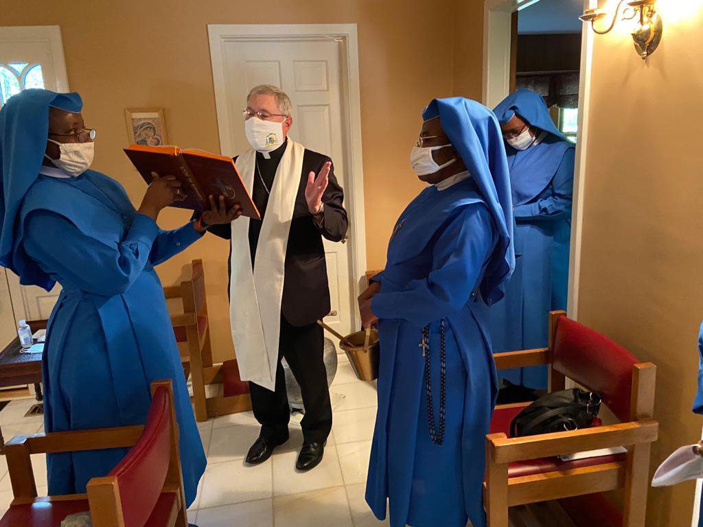 A priest and two altar servers in blue robes inside a church.