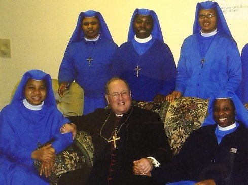 A group of nuns and a clergyman smiling indoors.