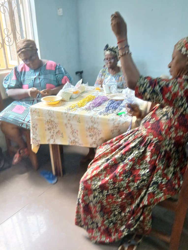 Three elderly women in colorful dresses sitting around a table sharing a meal.