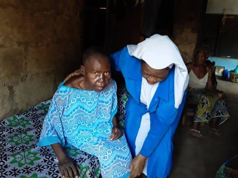 A woman in blue comforting an older woman in patterned clothing indoors.