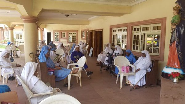 Group of elderly people socializing on a covered porch with caregivers.