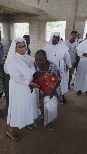 A nun embraces a young child holding a colorful bag, surrounded by other nuns.