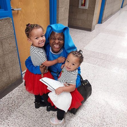 A joyful adult with two smiling toddlers in matching outfits.