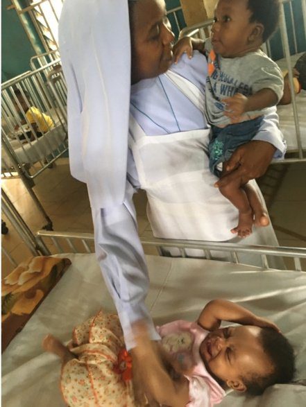 A man holding a baby lying on a hospital bed, another person gently touching the baby.