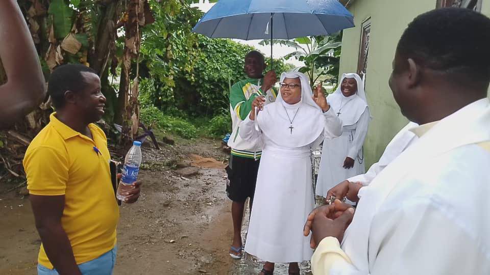Nuns holding umbrellas on a rainy path surrounded by greenery.