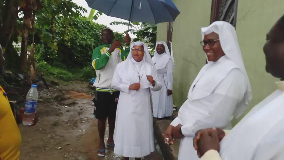 Nuns smiling and standing outdoors on a rainy day.